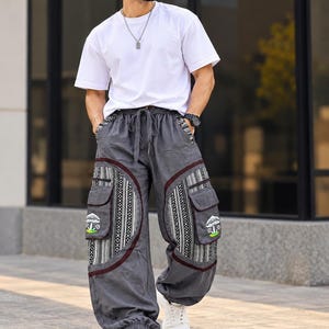 May include: A white short-sleeved t-shirt paired with loose-fitting charcoal gray cargo pants. The pants feature a drawstring waist, large side pockets with mushroom graphics, and vertical black and white patterned panels with dark red trim.