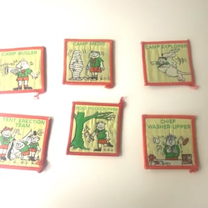 May include: Six square fabric patches with orange borders and light yellow backgrounds. Each patch features a cartoon character and text: CAMP BUGLER, CAMP MEDIC, CAMP EXPLORER, TENT ERECTION TEAM, HEAD WOODCHOPPER, and CHIEF WASHER-UPPER in green lettering.