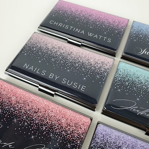 K&ouml;nnte beinhalten: Sechs verschiedene Visitenkartenhalter mit Glitzer-Design. Die Kartenhalter sind schwarz mit einem Farbverlauf aus rosa, blau, gr&uuml;n und lila Glitzer. Der Text auf den Kartenhaltern lautet "Christina Watts", "Nails by Susie", "Julie", "Heather", "Brenda" und "Ashley".