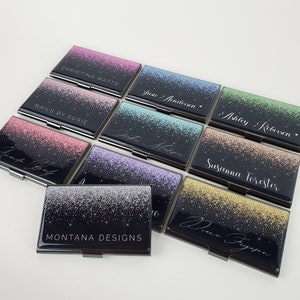 K&ouml;nnte beinhalten: Ein Set aus zehn schwarzen Visitenkartenhaltern mit silbernem Rand. Jeder Halter hat einen glitzernden Hintergrund in einer anderen Farbe und einen in Wei&szlig; gedruckten Namen. Die Namen sind: Christina Watts, Nails by Susie,  Justine Anderson,  Ashley Robinson,  Diana Ferguson,  Montana Designs,  Petra Hobson,  Susanna Forester,  und zwei weitere.