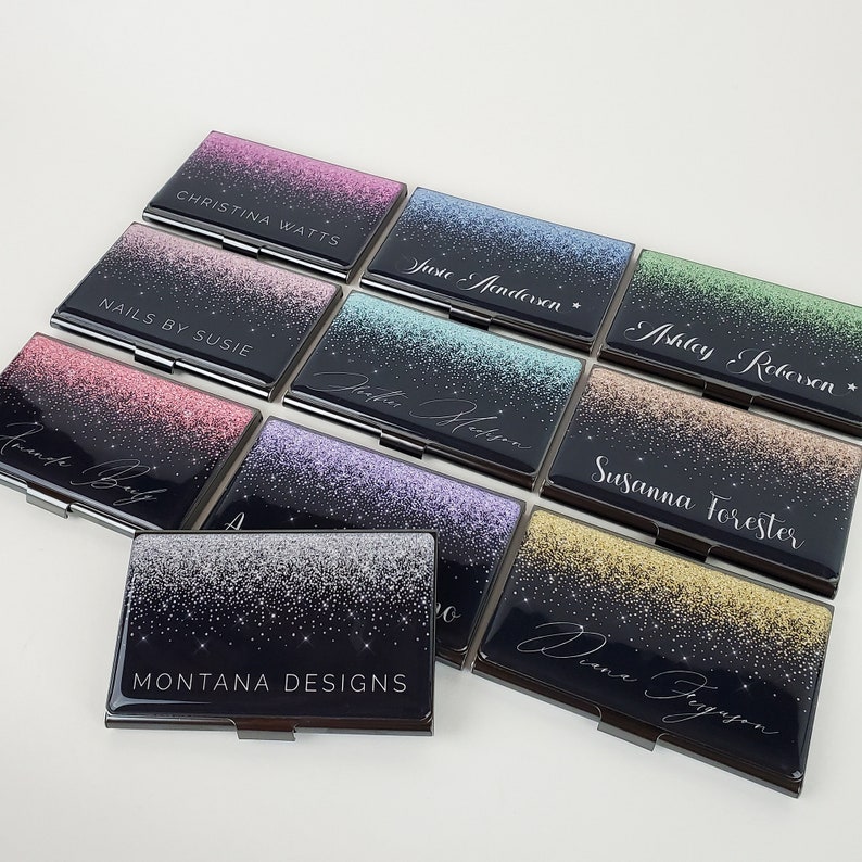 K&ouml;nnte beinhalten: Ein Set aus zehn schwarzen Visitenkartenhaltern mit silbernem Rand. Jeder Halter hat einen glitzernden Hintergrund in einer anderen Farbe und einen in Wei&szlig; gedruckten Namen. Die Namen sind: Christina Watts, Nails by Susie,  Justine Anderson,  Ashley Robinson,  Diana Ferguson,  Montana Designs,  Petra Hobson,  Susanna Forester,  und zwei weitere.