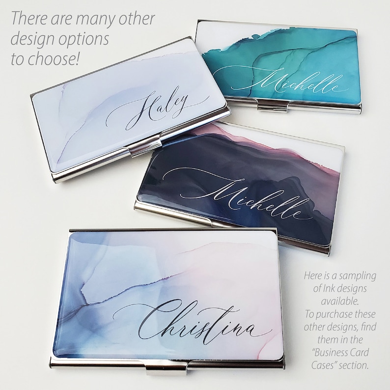 May include: Four silver business card holders with different watercolour designs and names printed on them. The designs include blue and green, blue and pink, and black and grey. The names are Haley, Michelle, Michelle, and Christina.