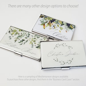 May include: Three silver business card holders with different floral designs. The top holder has a watercolour design of leaves and berries. The middle holder has a watercolour design of leaves and the text "Katherine Dawson". The bottom holder has a watercolour design of a wreath of leaves and the text "Christine Jackson".