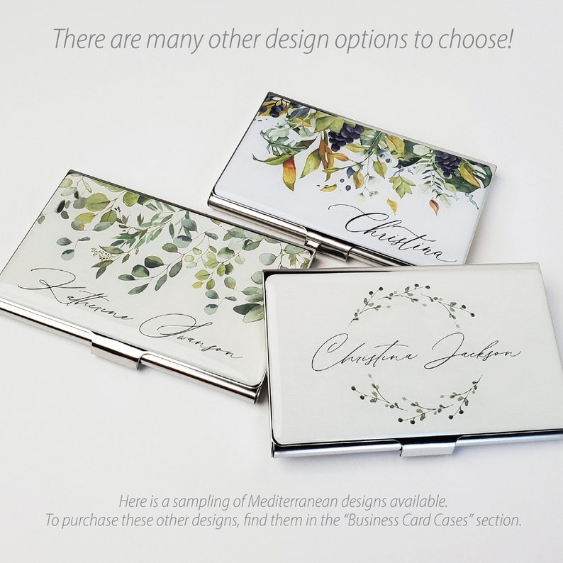 May include: Three silver business card holders with different floral designs. The top holder has a watercolour design of leaves and berries. The middle holder has a watercolour design of leaves and the text "Katherine Dawson". The bottom holder has a watercolour design of a wreath of leaves and the text "Christine Jackson".