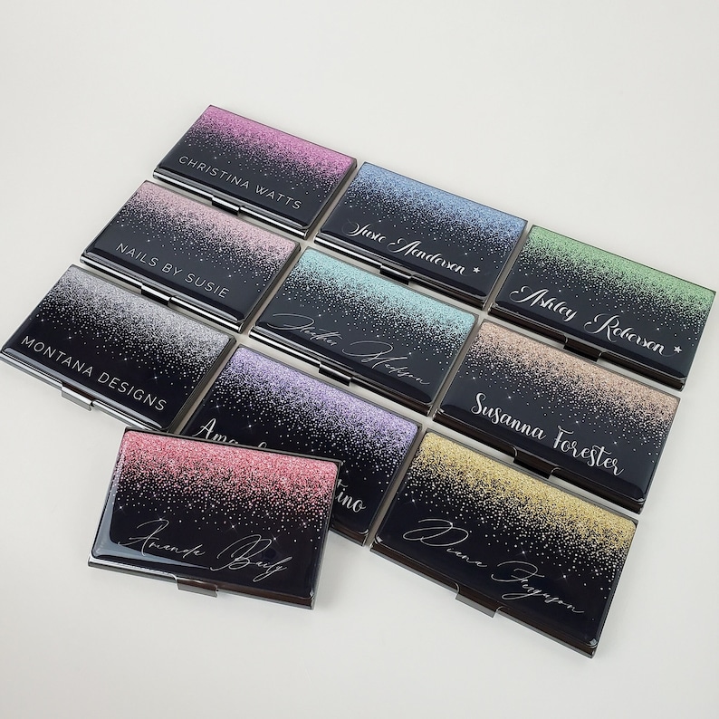 K&ouml;nnte beinhalten: Ein Set aus zehn Visitenkartenhaltern mit schwarzem Hintergrund und einem glitzernden, verlaufenden Design. Jeder Halter hat einen anderen Farbverlauf und einen in wei&szlig;er Schrift gedruckten Namen. Die Namen sind: Christina Watts, Just Rendersen, Ashley Rebersen, Nails by Susie, Montana Designs, Susanna Forester, Amanda Baily, Donna Fryggen, Victoria Shelton und Amino.