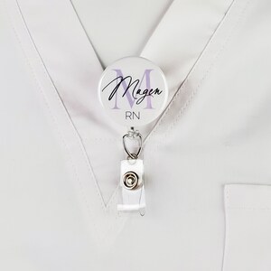 May include: White badge reel with a round, white button featuring a purple letter M and the text "Magen RN".