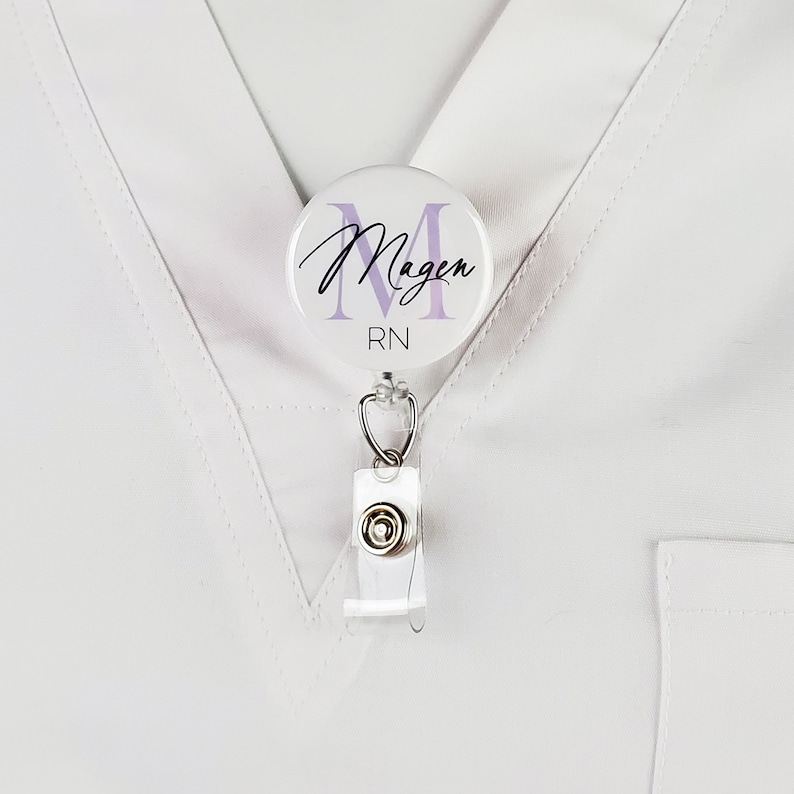 May include: White badge reel with a round, white button featuring a purple letter M and the text "Magen RN".