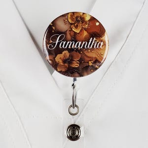 Puede incluir: Un carrete de identificaci&oacute;n con estampado floral marr&oacute;n y dorado con el nombre Samantha impreso en blanco.