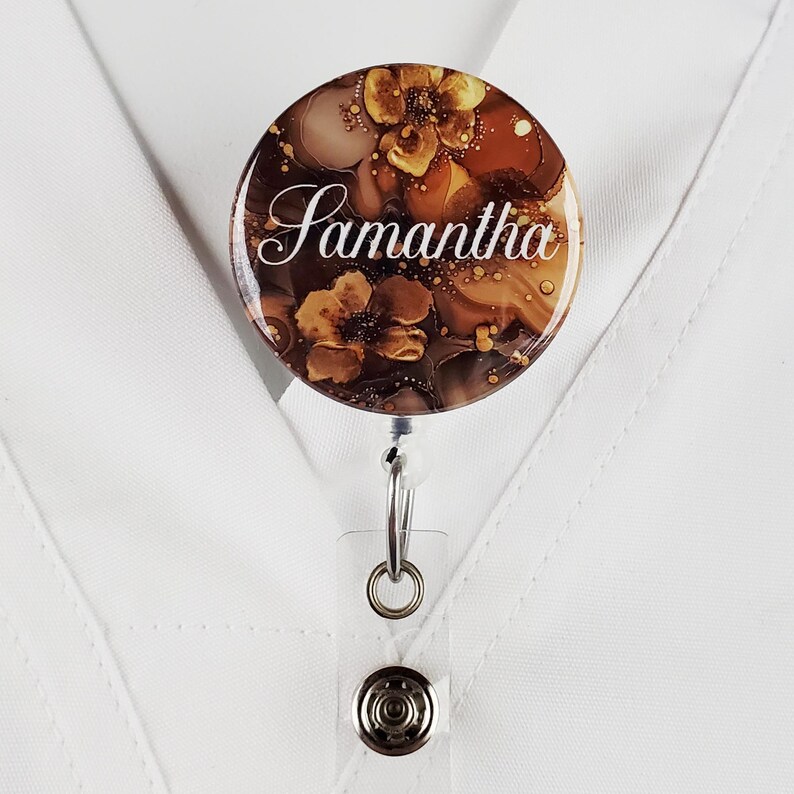 Puede incluir: Un carrete de identificaci&oacute;n con estampado floral marr&oacute;n y dorado con el nombre Samantha impreso en blanco.