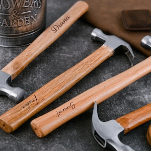 May include: A collection of four claw hammers with polished silver metal heads and light brown wooden handles. Each handle features a unique name engraved in a dark cursive script, including the names Diana, Trisha, and Simrat on the visible handles.