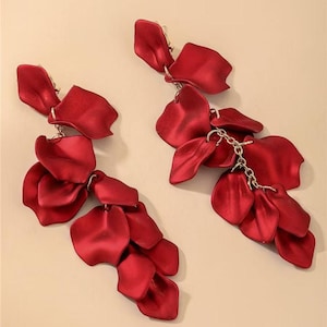 May include: A pair of long drop earrings featuring multiple deep red, matte-finish petal shapes attached to thin gold-tone metal chains. The petals are layered and arranged in a cascading design, creating a floral-inspired look with a smooth texture.