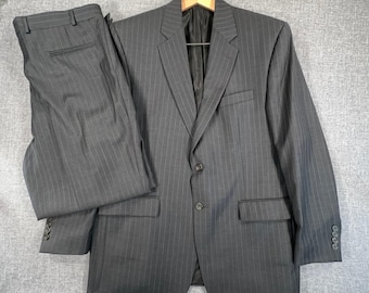 Può includere: Un completo due pezzi grigio antracite con un sottile motivo a righe verticali. Il set comprende una giacca monopetto con due bottoni, revers classici e pantaloni abbinati con fascia in vita e passanti per cintura.