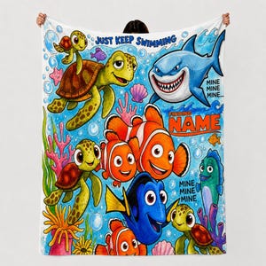 Puede incluir: Una manta de forro polar con una escena submarina vibrante que muestra tortugas marinas, peces payaso, un pez cirujano azul y un tiburón. El texto dice JUST KEEP SWIMMING, MINE MINE MINE y FINDING NAME, con coral y burbujas sobre fondo azul.