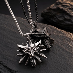 May include: Two metal necklaces featuring stylized wolf head pendants. One pendant is polished silver-tone metal on a matching silver-tone chain, while the other is matte black metal on a matching black chain. Both pendants have sharp, angular features.
