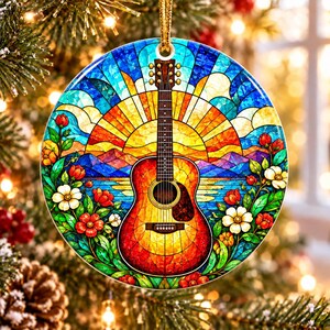 May include: A round ceramic ornament featuring a stained glass style illustration of an acoustic guitar centered in front of a vibrant sunset, mountains, and water, framed by colorful red and white flowers and green leaves.