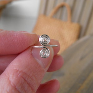 May include: A silver ring with two spiral designs. The ring is made of wire and is a simple, minimalist design.