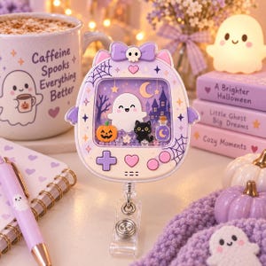 May include: A purple and white handheld game-shaped badge reel featuring a ghost, a black cat, a pumpkin, and a potion bottle inside a liquid-filled shaker window. The top has a purple bow with a skull, and the device includes a metal clip.