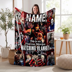 May include: A rectangular fleece blanket featuring a collage of various horror movie characters and scenes. The text NAME is printed at the top, and the text This is my Horror Movies WATCHING BLANKET is printed in the center in white lettering.