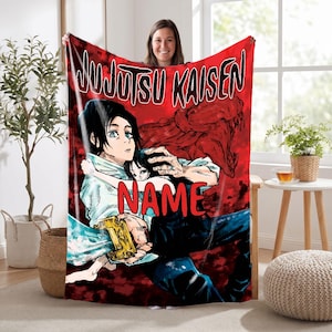 Peut inclure: Une couverture rectangulaire en polaire avec un fond rouge vif et le logo Jujutsu Kaisen en haut. L'illustration représente deux personnages d'anime dans une pose dynamique avec une épée, et le mot NAME écrit en grandes lettres rouges.