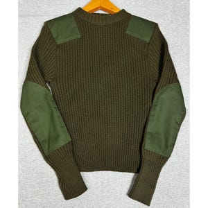 May include: An olive green ribbed knit sweater featuring solid fabric patches on the shoulders and elbows. The long-sleeved garment has a crew neckline and a vertical ribbed texture throughout the body and sleeves, providing a uniform appearance.