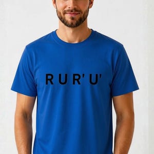 May include: A vibrant blue short-sleeved t-shirt featuring the text RUR'U' printed in bold black capital letters across the chest. The garment has a classic crew neckline and a straight hem, providing a clean and simple look for casual wear.
