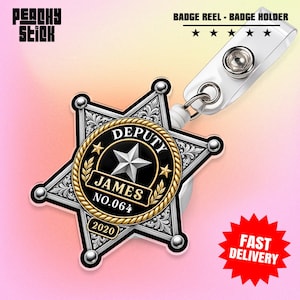 May include: A star-shaped badge reel featuring a silver sheriff-style star with ornate engravings. The center is a black circle with a gold rope border, displaying the text DEPUTY, JAMES, NO.064, and 2020. It includes a white plastic clip.