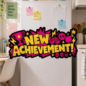 May include: A large, vibrant sticker featuring the text NEW ACHIEVEMENT! in bold yellow letters with a black outline. The design includes pink and yellow graphic elements like a trophy, a skull, a bomb, lightning bolts, and a tiara with glasses.