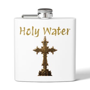 May include: A white metal flask with a silver screw-top cap. The front features the gold-colored text Holy Water above a detailed, ornate, bronze-toned gothic cross design. The flask has a smooth, matte finish and a rectangular shape.