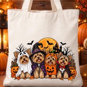 May include: A cream-coloured canvas tote bag featuring a graphic print of four Yorkshire Terrier dogs dressed in Halloween costumes, including a ghost, a witch, a pumpkin, and a vampire, set against a backdrop of a full moon and a haunted house.