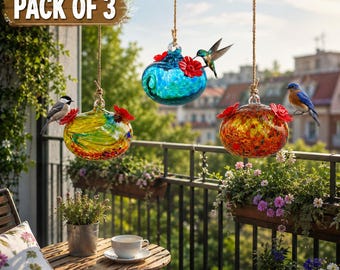 Könnte beinhalten: Ein Dreierpack hängender Kolibri-Futterstellen aus Glas mit roten, blütenförmigen Futteröffnungen. Die Futterstellen verfügen über farbenfrohe, gewirbelte Glasdesigns in Blau, Gelbgrün und Orangerot, die an braunen Kordeln hängen.