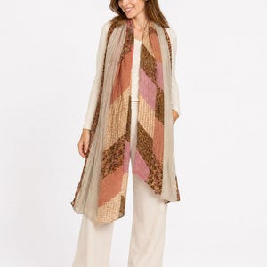 Puede incluir: Una bufanda rectangular larga con un diseño de patchwork de rayas diagonales en tonos marrón, rosa y beige con patrones florales y texturizados, sobre una blusa color crema de manga larga y pantalones anchos a juego con zapatos marrones.