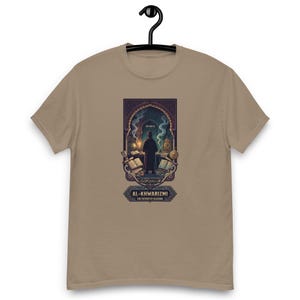 Może przedstawiać: Beżowy t-shirt z grafiką przedstawiającą osobę stojącą w łukowatym gabinecie pełnym książek i zwojów. Tekst pod ilustracją brzmi AL-KHWARIZMI THE FATHER OF ALGEBRA i znajduje się w ozdobnej niebiesko-złotej ramce.