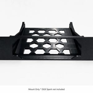 May include: A black rack mount shelf featuring a flat base with a hexagonal cutout pattern and two side support brackets. The front panel includes four mounting holes. The text at the bottom reads: Mount Only * DGX Spark not included.