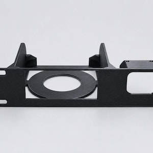 May include: A black rack-mount panel featuring a circular cutout in the center, a square cutout on the right side, and four mounting holes at the corners. The structure includes two vertical support fins extending backward from the main faceplate.