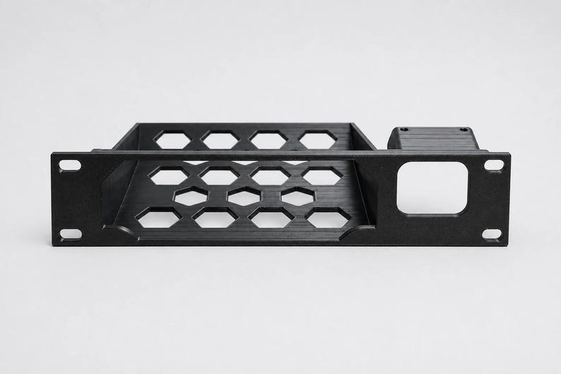 K&ouml;nnte beinhalten: Ein schwarzes Rack-Montage-Regal mit einem sechseckigen Wabenmuster auf der Basis zur Bel&uuml;ftung. Die Frontplatte verf&uuml;gt &uuml;ber vier Befestigungsl&ouml;cher und einen quadratischen Ausschnitt auf der rechten Seite f&uuml;r die Rack-Installation.