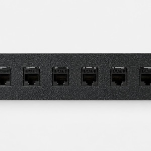Pode incluir: Um painel de conex&atilde;o preto retangular para montagem em rack com oito portas Ethernet RJ45 individuais rotuladas como Cat6. O painel inclui quatro orif&iacute;cios de montagem, um em cada canto, projetados para instala&ccedil;&atilde;o segura em racks.