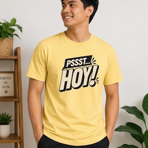 May include: A light yellow short-sleeved t-shirt featuring a black graphic print on the chest. The design includes the text PSSST... and HOY! in a bold, comic-book style font with a black speech bubble background and decorative accent lines.