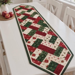 May include: A rectangular quilted table runner featuring a geometric pattern of red, dark green, and cream fabric blocks. The design includes festive prints of poinsettias, holly leaves, and snowflakes, finished with a dark green border trim.
