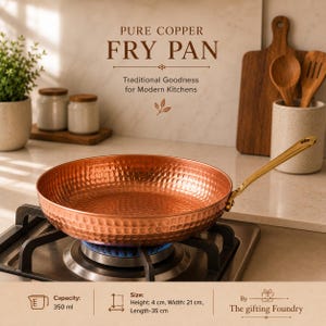 May include: A hammered copper fry pan with a gold-toned handle resting on a gas stove burner. The text reads: PURE COPPER FRY PAN, Traditional Goodness for Modern Kitchens, Capacity: 350 ml, Size: Height: 4 cm, Width: 21 cm, Length: 35 cm, By The gifting Foundry.