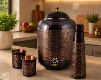 May include: A dark-toned metal water dispenser with a gold-colored lid knob and a silver spigot, accompanied by two matching tumblers and a tall water bottle. Each piece features an intricate, repeating copper-colored floral pattern.