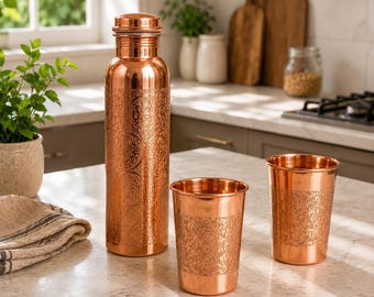 May include: A tall, cylindrical copper water bottle with a screw-top lid and two matching copper tumblers. Each item features an intricate, repeating floral pattern etched into the metallic surface, showcasing a polished, warm copper finish.