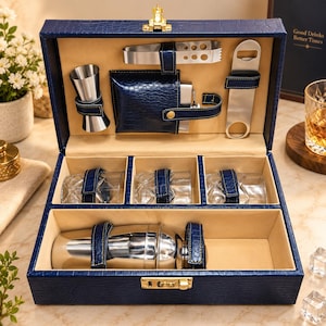 May include: A navy blue crocodile-textured leatherette bar set case with a gold latch. The interior features a stainless steel jigger, ice tongs, bottle opener, flask, three crystal-cut whiskey glasses, and a cocktail shaker, all secured by straps.