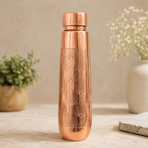 Könnte beinhalten: Eine zylindrische Wasserflasche aus Kupfer mit einem sich wiederholenden, geprägten Muster aus fächerförmigen Blättern. Die Flasche hat eine glatte, metallische Oberfläche und einen passenden Schraubverschluss in einem warmen, rötlich-braunen Farbton.
