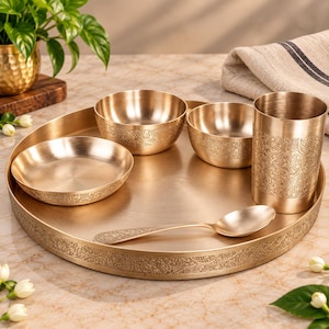 Puede incluir: Un juego de vajilla de latón que consta de una bandeja redonda grande, dos cuencos pequeños, un plato hondo, un vaso alto y una cuchara. Cada pieza presenta un grabado floral detallado a lo largo del borde o la superficie exterior.
