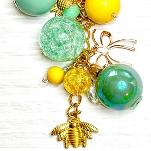 May include: A gold charm bracelet with green and yellow beads, a gold bee charm, and a gold honeycomb charm.