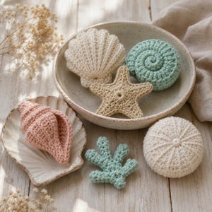 Puede incluir: Una colección de artículos marinos tejidos a ganchillo que incluye una concha de vieira color crema, una concha en espiral verde menta, una estrella de mar color canela, una caracola rosa, un trozo de coral verde claro y un erizo de mar blanco redondo.