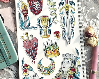 以下が含まれることがあります： 白い紙に描かれたカラフルな手描きイラストのコレクション。イラストには、ブドウのついたハート、王冠、剣、聖杯、頭蓋骨、松明、盾、目のある三日月、そして王冠をかぶった女性の顔などが含まれています。