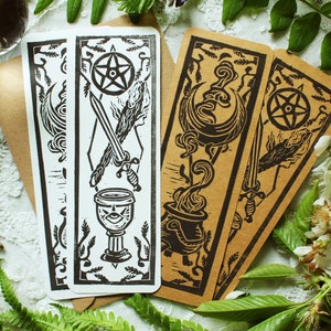 May include: Three brown paper bookmarks with black ink illustrations of a sword, a cauldron, and a chalice. Each bookmark features a pentagram and other decorative elements.
