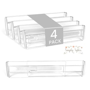 May include: A four-pack of clear, adjustable drawer dividers made of transparent plastic. Each divider features a sliding mechanism with a ridged grip for length adjustment. A grey band wraps around the set with the text 4 PACK printed in white.
