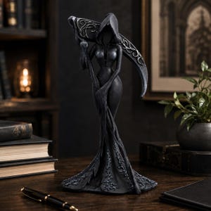 May include: A dark gray, hooded figurine of a slender, faceless figure standing upright. The figure wears a long, flowing gown with intricate floral detailing at the hem and holds a large, curved scythe with ornate silver-toned filigree patterns.